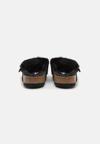 Black slippers featuring a soft fur interior, a brown cork outer sole, and textured rubber bottom. Rounded shape with a simple design.
