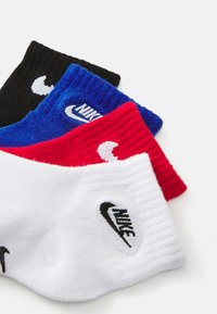 Cuatro pares de calcetines Nike en negro, azul, rojo y blanco, con textura acanalada y bordado del logo en cada calcetín.