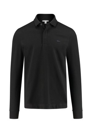 Mann trägt schwarze und weiße Zip-up-Jacke, schwarzes Poloshirt, schwarze Hose mit weißen Seitenstreifen und schwarz-weiße Sneakers.