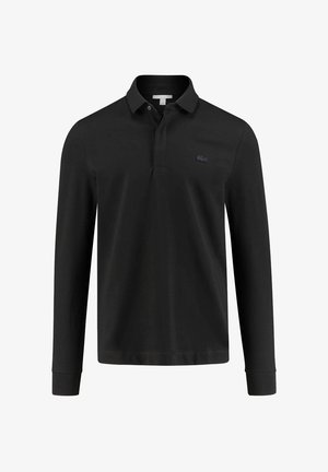 Mann trägt schwarze und weiße Zip-up-Jacke, schwarzes Poloshirt, schwarze Hose mit weißen Seitenstreifen und schwarz-weiße Sneakers.
