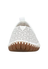 Weißer Slipper mit ausgeschnittenen geometrischen Mustern. Glattes Obermaterial, Gummisohle mit strukturiertem braunem Boden und kontrastierenden Nähten.