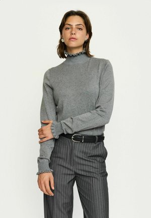 Hele halli kudumisturtleneckiga sviiter, millel on volangiga kaelus ja mansetid, kantud hallide triibuliste pükstega ja musta vööga.