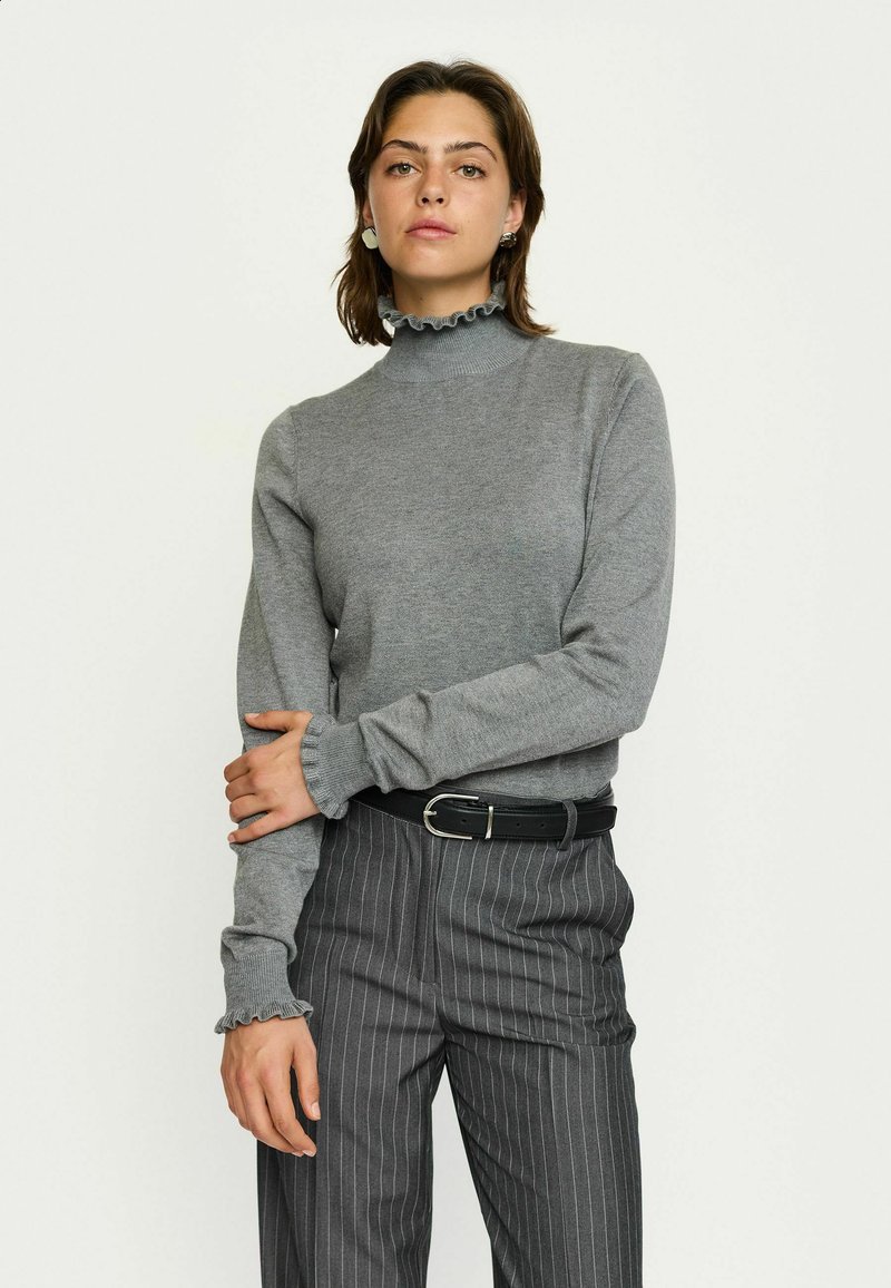 Maglione a collo alto grigio chiaro in maglia con colletto e polsini arricciati, indossato con pantaloni grigi a righe e una cintura nera.