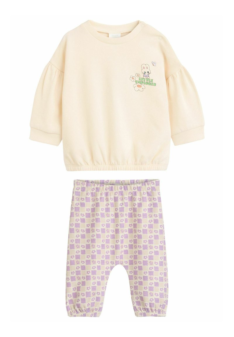 Hanorac bej deschis cu mâneci bufante și un grafic cartoon, asociat cu pantaloni cu carouri lavandă care au un model floral.