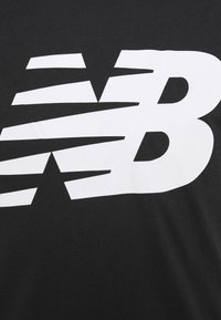 Camiseta negra de algodón con un gran logo blanco de New Balance y varios rayas inclinadas integradas en el diseño. Textura suave.