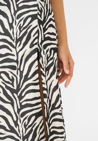 Maxikleid mit einem schwarz-weißen Zebramuster, ausgestattet mit einem seitlichen Reißverschluss und einer eleganten, glatten Stoffoberfläche.