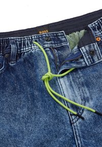 Džínové šortky s kombinací tmavě a světlomodrých odstínů, elastickým pasem s zelenou šňůrkou a viditelnou značkovou etiketou.