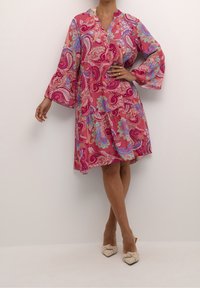 Różowa sukienka w paisley z długimi, rozkloszowanymi rękawami i luźnym fasonem. Wykonana z lekkiego materiału, z dekoltem w kształcie litery V i marszczeniami.