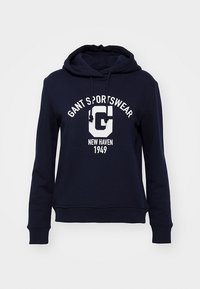 Sweat à capuche bleu marine avec cordons de capuche, inscription blanche "GANT SPORTSWEAR", grand "G" et texte "NEW HAVEN 1949" sur le devant.