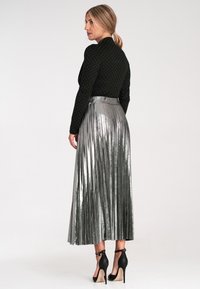Czarna bluzka z długim rękawem w białe kropki, połączona z metalicznie srebrną, plisowaną spódnicą maxi oraz czarnymi szpilkami z paskami na kostkach.