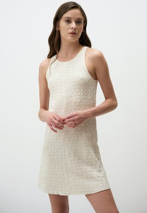 Vestito senza maniche in tessuto crema testurizzato con silhouette aderente, caratterizzato da scollatura rotonda e orlo al ginocchio.