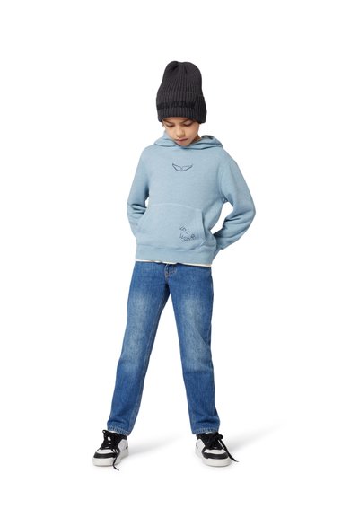 Sweatshirt à capuche bleu clair avec une poche avant, orné de broderies sombres. Associé à un jean en denim bleu et à des baskets noires et blanches.