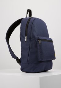 Sac à dos en tissu bleu marine avec une forme arrondie, doté d'une poche zippée à l'avant, de bretelles ajustables et de détails en maille au dos.