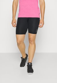 Pantaloni sportivi neri abbinati a una maglietta a maniche corte rosa. Caratteristiche includono un design aderente e accenti di logo discreti sui pantaloni.