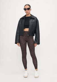 Crna umjetna kožna cropped jakna, crni cropped top, smeđe tajice s crnim leopard uzorkom, bijele platforme, crne sunčane naočale.
