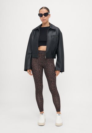 Zwarte neplederen cropped jacket, zwarte cropped top, bruine legging met zwart luipaardprint, witte platform sneakers, zwarte zonnebril.