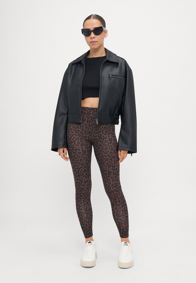 Crna umjetna kožna cropped jakna, crni cropped top, smeđe tajice s crnim leopard uzorkom, bijele platforme, crne sunčane naočale.