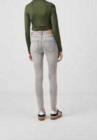 Vaqueros skinny grises con una textura suave, diseño de cinco bolsillos y detalles de costura sutiles. Llevados con una camiseta de manga larga verde ajustada y zapatos negros.