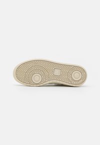 Gummisko sål i beige med et fiskebensmønster og cirkulære detaljer. Tekstureret greb og brandlogo synligt.
