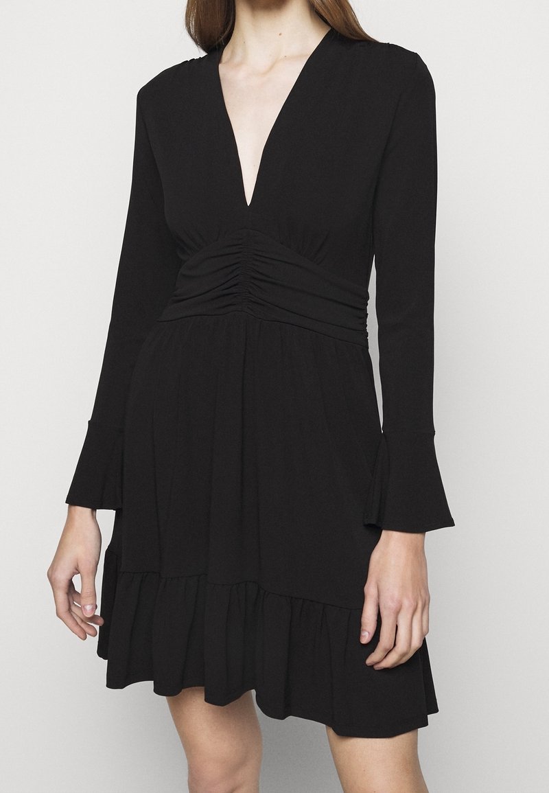 Vestito nero con maniche lunghe, scollatura a V, corpetto arricciato e orlo a balze. Realizzato in un tessuto morbido con una silhouette fluida.