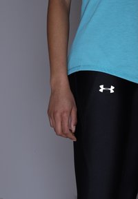 Svarta leggings med en vit Under Armour-logga, i kombination med en ljusblå, kortärmad t-shirt i bomull, som visar en figurnära siluett.