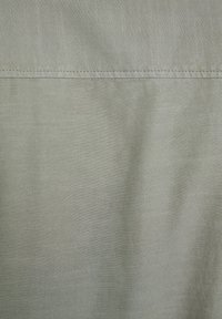 Jasnoszara tkanina o teksturowanym splocie i subtelnych pionowych paskach. Zakończenie przypięte z widocznym detalem szycia. Miękka i gładka powierzchnia.