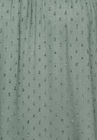 Tessuto verde con texture caratterizzato da punti in rilievo disposti in un motivo regolare, con una finitura liscia che riflette leggermente la luce.