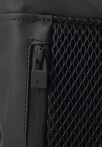 Black backpack featuring a smooth, matte surface, mesh details, and a zipper pull with a star pattern. Stitched accents in matching color.