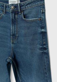 Blauwe denim jeans met een gladde textuur, ontwerp met vijf zakken, gestikte details en een metalen knoopsluiting bij de tailleband. Maatlabel zichtbaar.