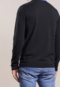 Black long-sleeve shirt with a classic crew neck, made of lightweight fabric, paired with blue jeans featuring a standard five-pocket design.