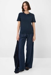 Marineblaues T-Shirt mit kurzen Ärmeln und Rundhalsausschnitt, aus weichem Stoff. Kombiniert mit weit geschnittenen Jeans und einem dunklen Pullover.