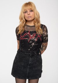 Black mesh t-shirt with a faded splatter pattern, featuring the word "SLAYER" in red. Paired with a high-waisted black denim skirt.