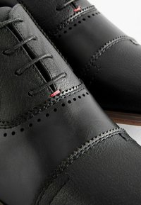 Zapatos de cuero negro con una textura suave, que presentan costuras decorativas, acentos perforados y cordones rojos en contraste.