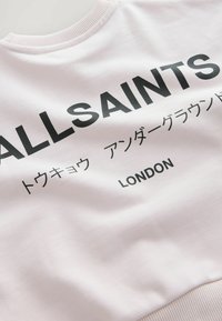 Biała bluza z kapturem z czarnym napisem "ALLSAINTS", japońskimi znakami i "LONDYN", pokazująca kołnierz i część górnej tylnej części.