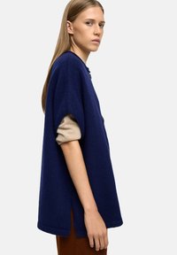Granatowy, oversize sweter z krótkimi rękawami, z beżowymi podwinięciami i bocznymi rozcięciami, wykonany z fakturowanej tkaniny i o luźnym kroju.