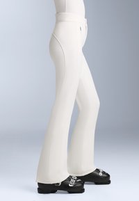 Fehér, széles szárú nadrág sima textúrával, magas derékkal és látható varrással, fekete lábbelivel, ezüst hardware-rel párosítva.