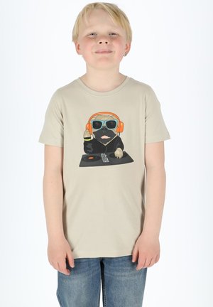 Beige puuvillainen t-paita, jossa on graafinen kuva koirasta, joka käyttää oransseja kuulokkeita, aurinkolasit ja mustaa DJ-levylautasta kuvaava design. Yhdistetty farkkuihin.