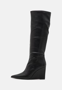 Botte noire en cuir montant jusqu'au genou avec un bout pointu et un talon compensé. Texture lisse et design supérieur plié créent une silhouette épurée.