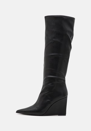 Botte noire en cuir montant jusqu'au genou avec un bout pointu et un talon compensé. Texture lisse et design supérieur plié créent une silhouette épurée.