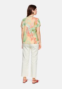 Kurzärmliges Oberteil mit Blumenmuster in Pastellfarben, kombiniert mit weißen, weiten Hosen. Verfügt über eine lockere Passform und einen weichen, leichten Stoff.