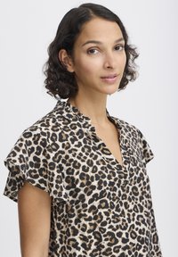 Blouse imprimée léopard avec des manches courtes à volants, présentant un décolleté en V dans des tons de noir et de marron sur un fond clair.