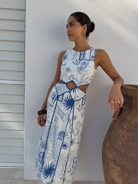 Rochie maxi din material alb, cu ilustrații imprimate în albastru. Design cu decupaje, fără mâneci, cu o fustă fluidă și modele intricate.