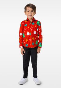 Camisa roja abotonada con varios estampados festivos, incluyendo muñecos de nieve, renos y árboles de Navidad, combinada con pantalones negros y zapatos blancos.