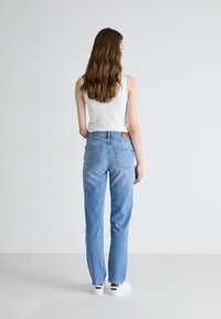 Light blue high-waisted jeans with a straight cut, featuring back pockets and a brown leather patch at the waist, paired with a white top.