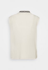 Haut sans manches crème à finition texturée, avec un col brodé noir. Coupe droite avec fentes latérales pour une meilleure aération.