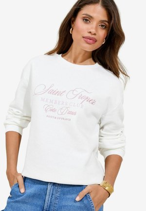 Weißer Sweater mit langen Ärmeln, der pinken Schrift "Saint Tropez Members Club Côte d'Azur Südfrankreich" zeigt. Weicher Stoff.