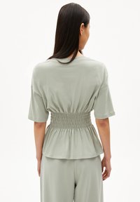 Hellgrünes, gerafftes Oberteil mit kurzen Ärmeln, lockerer Passform und geraffter Textur an der Taille. Weicher, glatter Stoff.