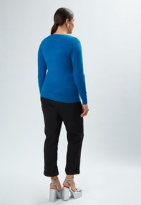 Blauw langemouwen shirt met een fitted design, gecombineerd met zwarte opgerolde broek en zilveren platformhakken, met een gladde textuur.