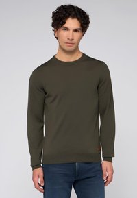 Tmavě zelený pletený svetr s dlouhými rukávy, žebrovaným kulatým výstřihem a manžetami, vyrobený z texturované tkaniny, s malou hnědou koženou visačkou na dolním lemu.