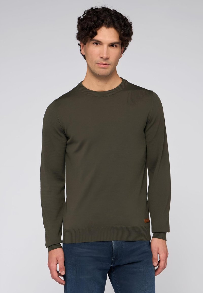 Tmavě zelený pletený svetr s dlouhými rukávy, žebrovaným kulatým výstřihem a manžetami, vyrobený z texturované tkaniny, s malou hnědou koženou visačkou na dolním lemu.